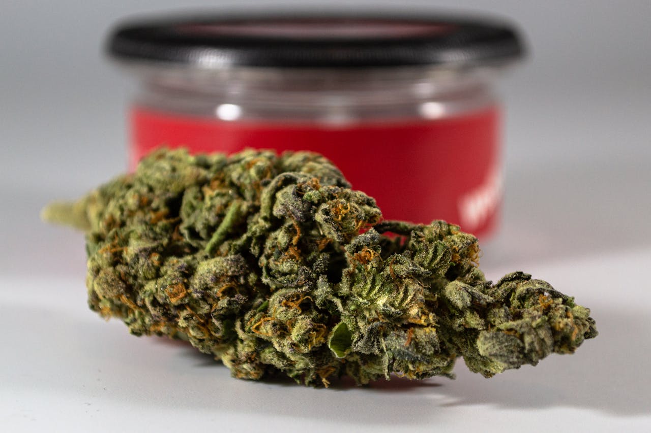 Macro photo of a cannabis bud with a blurred red container in the background.